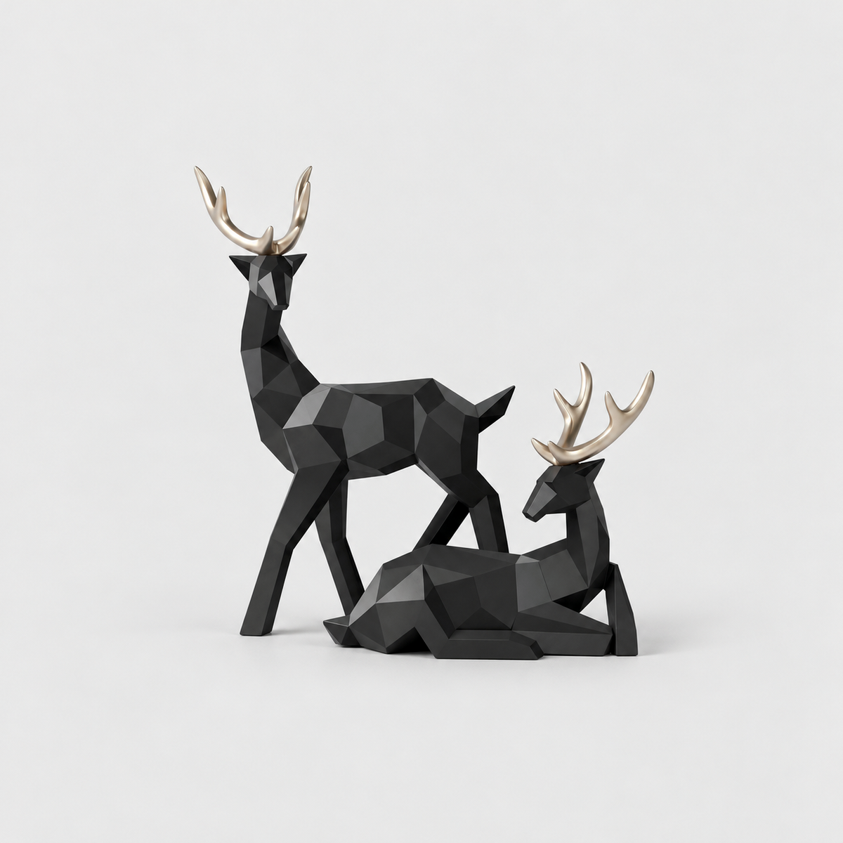 Pair of black geometric faceted reindeer sculptures with gold antlers, one standing and one lying down, on a light gray background