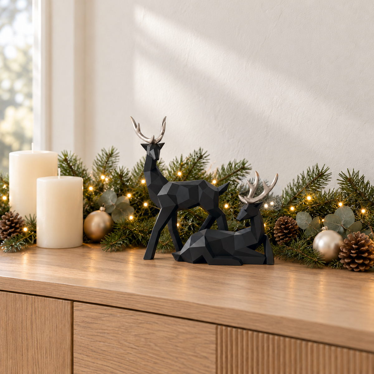 Black geometric reindeer sculptures with gold antlers on a pale oak sideboard beside a fir garland with warm fairy lights