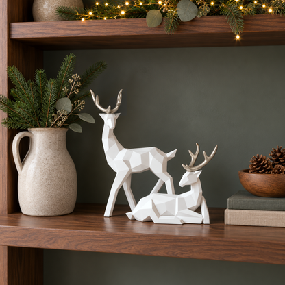 White geometric reindeer sculptures with gold antlers on a dark walnut shelf beside books and pine cones with fairy lights