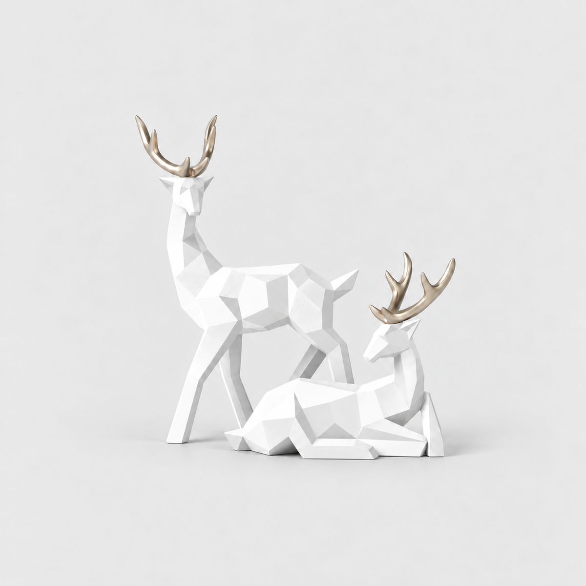 Pair of white geometric faceted reindeer sculptures with gold antlers on a light gray background