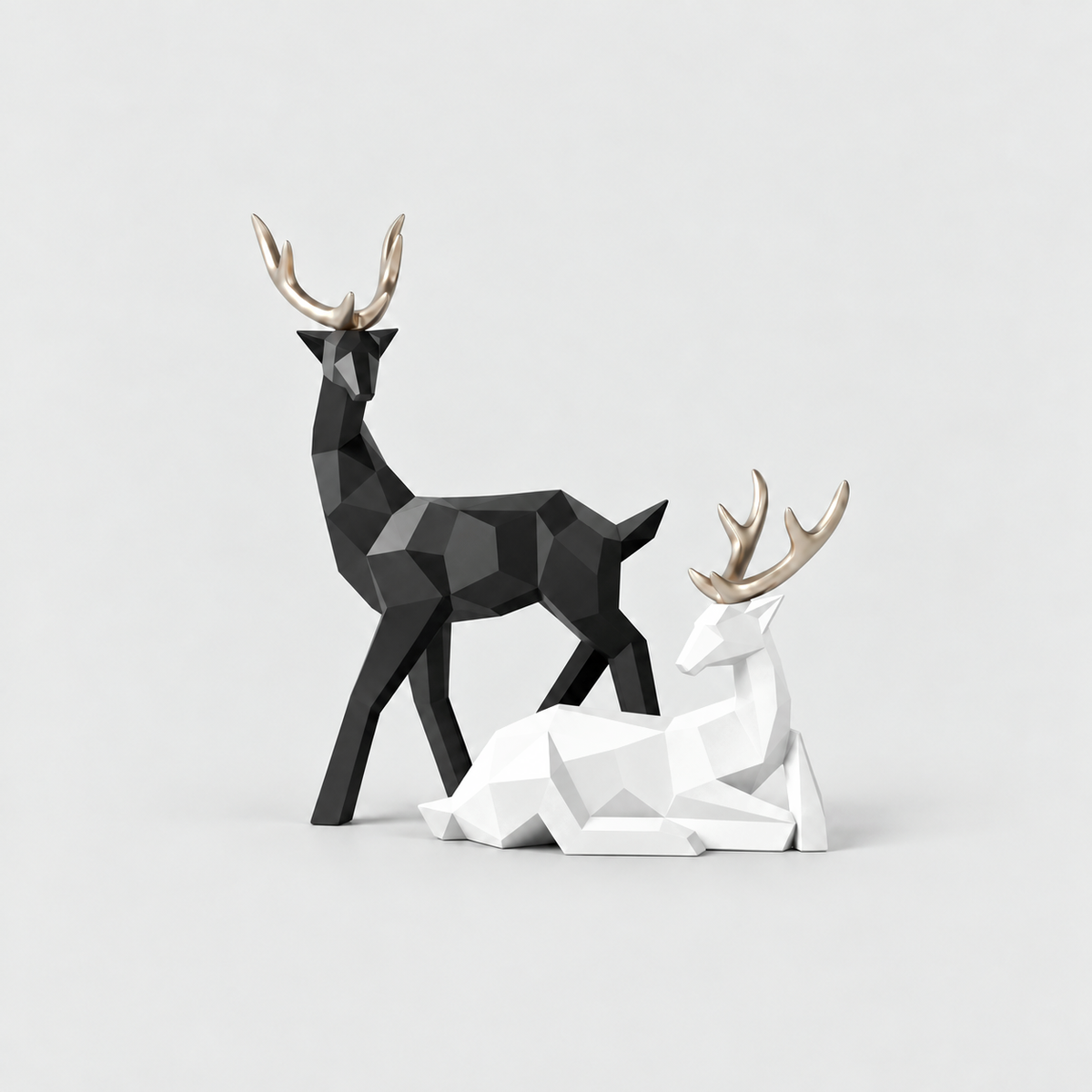 Black standing reindeer sculpture and white lying reindeer sculpture with gold antlers on a light gray background