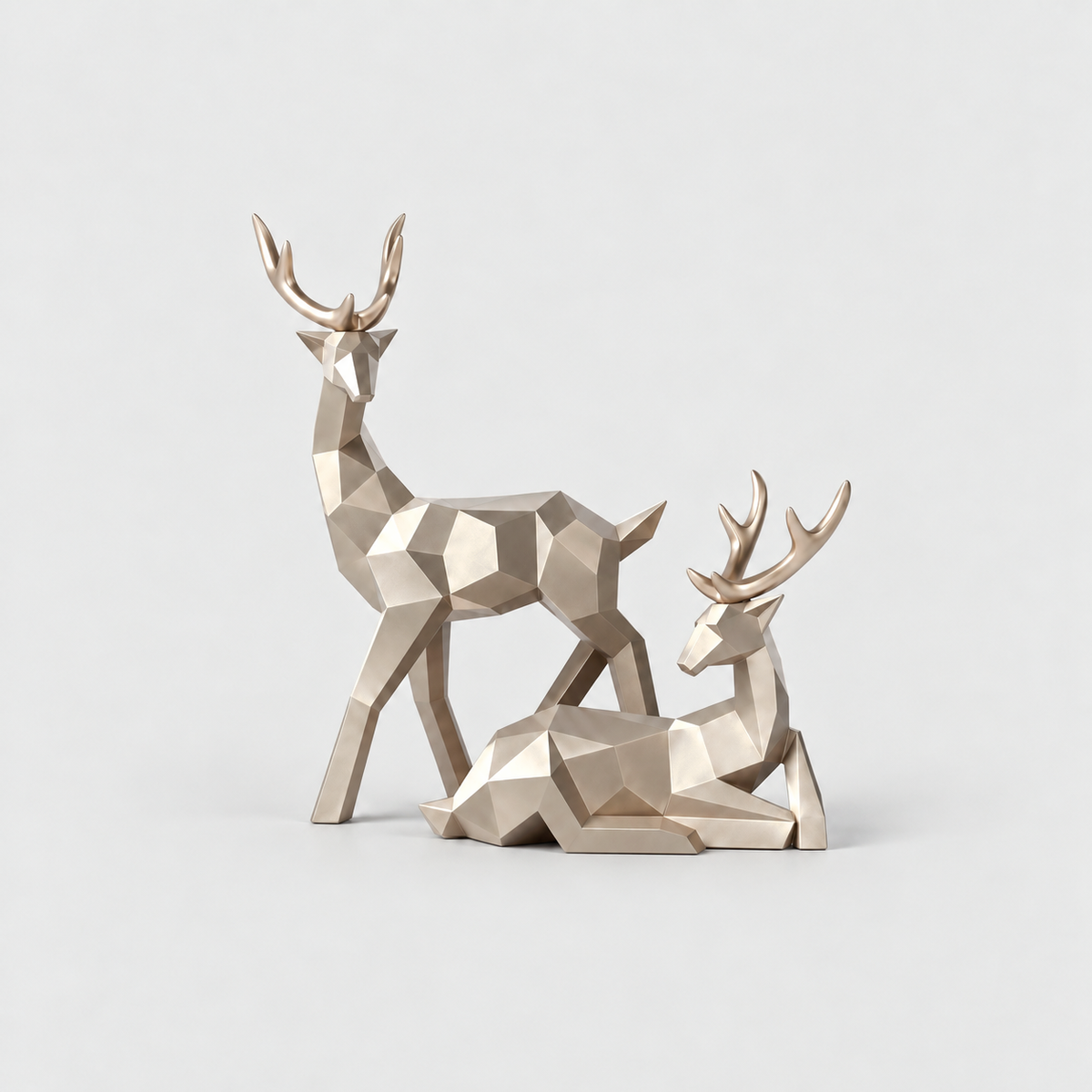 Pair of champagne gold geometric faceted reindeer sculptures, one standing and one lying, on a light gray background