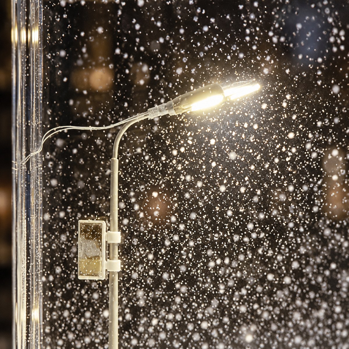 Close-up of the miniature street lamp glowing warm white inside the block with snowflakes drifting past