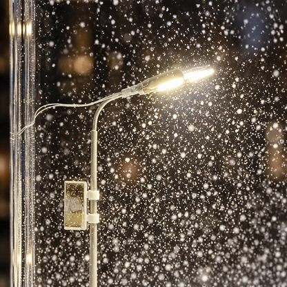 Close-up of the miniature street lamp glowing warm white inside the block with snowflakes drifting past