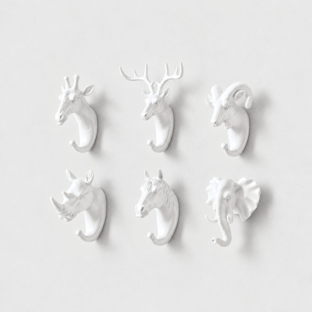 Six white animal head wall hooks, giraffe, deer, ram, rhino, horse and elephant, on a plain light gray wall