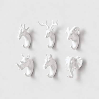 Six white animal head wall hooks, giraffe, deer, ram, rhino, horse and elephant, on a plain light gray wall