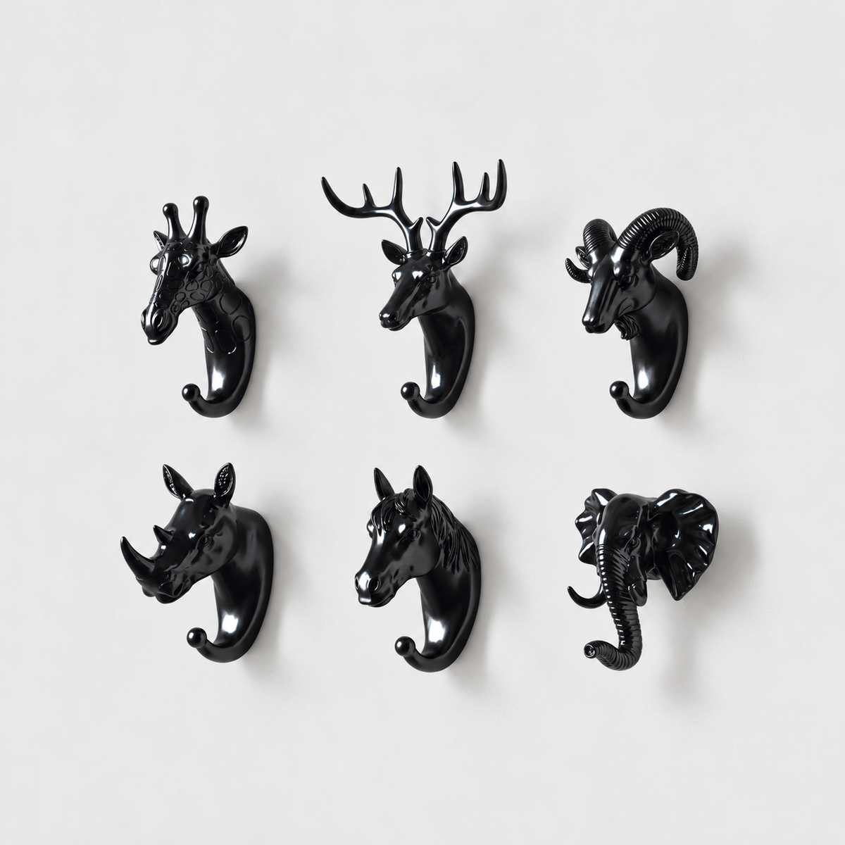 Six black animal head wall hooks, giraffe, deer, ram, rhino, horse and elephant, on a plain light gray wall