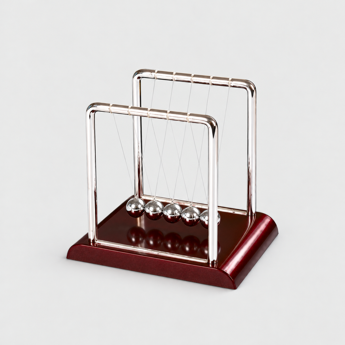 Newton's cradle desk ornament with two polished steel frames, five steel balls and a glossy wine red base on a light gray background