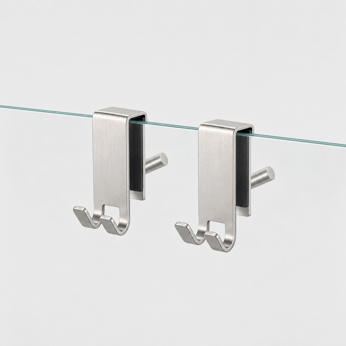 Two brushed silver stainless steel shower door hooks clipped over the top edge of a clear glass panel, on a light gray background