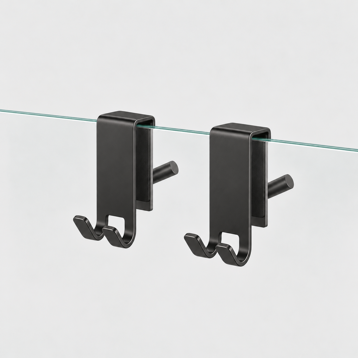 Two charcoal black stainless steel shower door hooks clipped over the top edge of a clear glass panel, on a light gray background