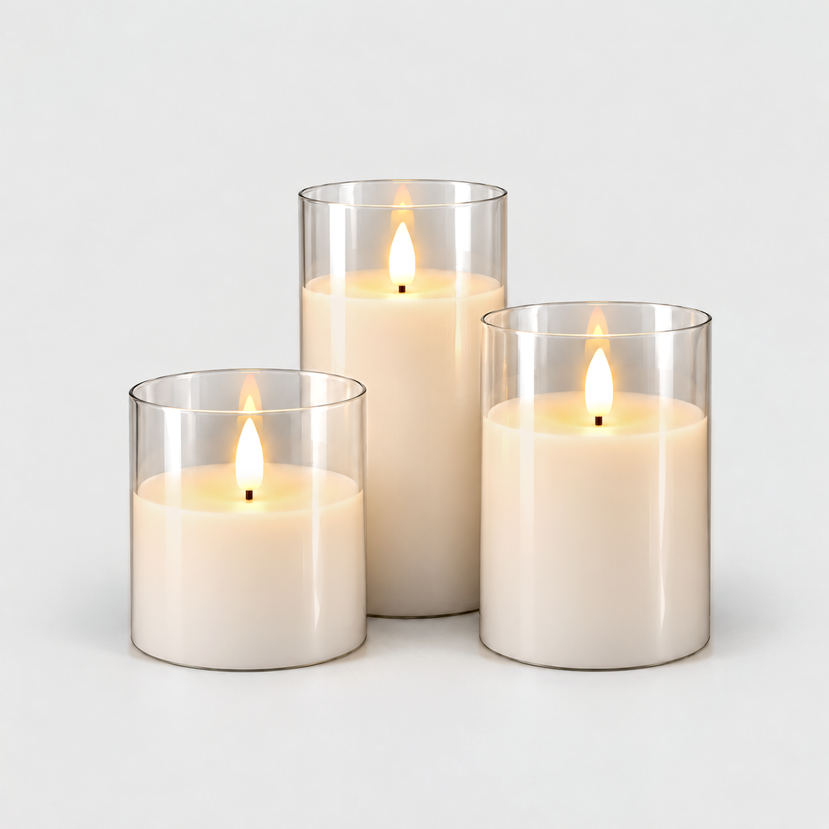Three flameless LED pillar candles in clear glass sleeves, lit, in three heights