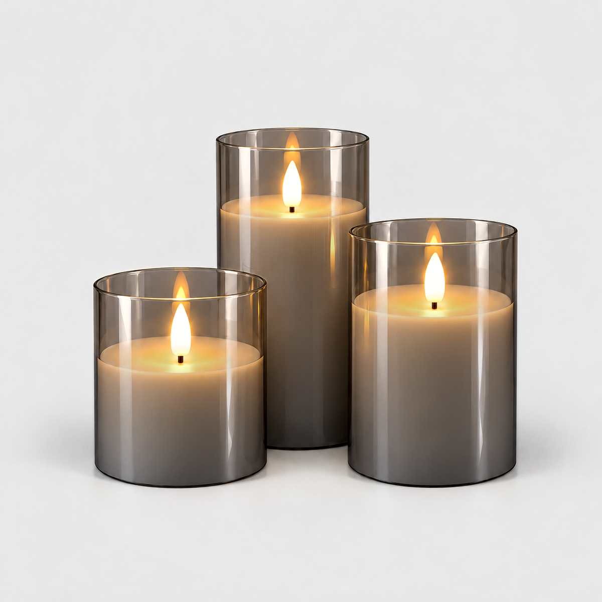Three flameless LED pillar candles in smoked gray glass sleeves, lit, in three heights