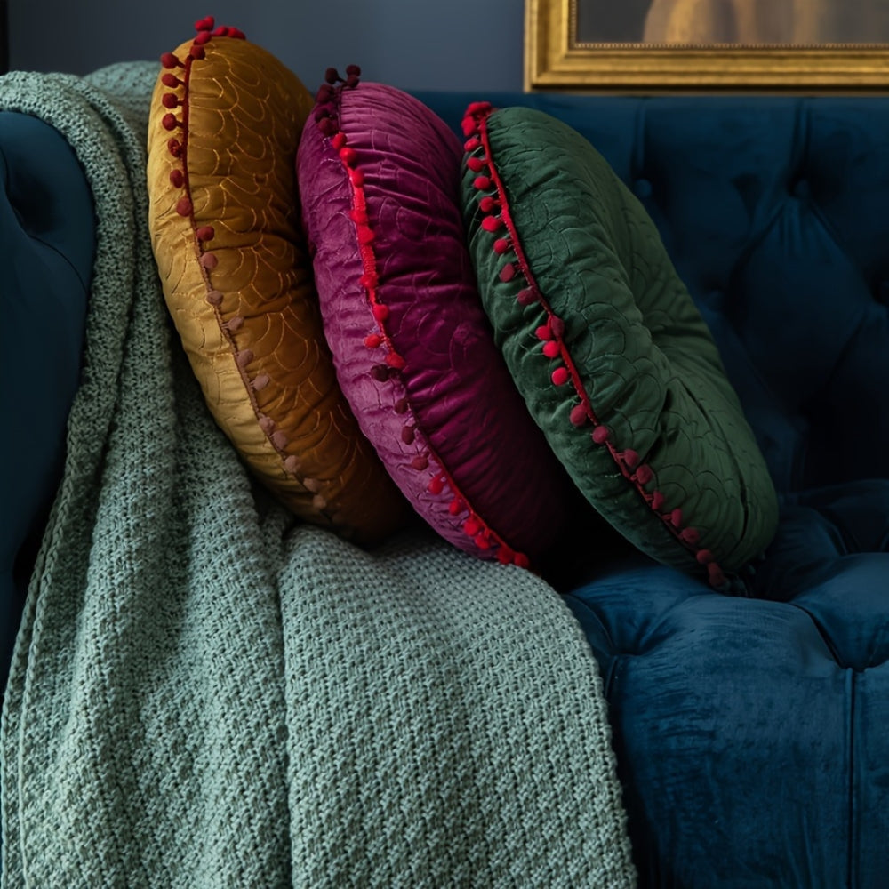 Three round velvet cushions in mustard, plum and green leaning on a navy velvet sofa