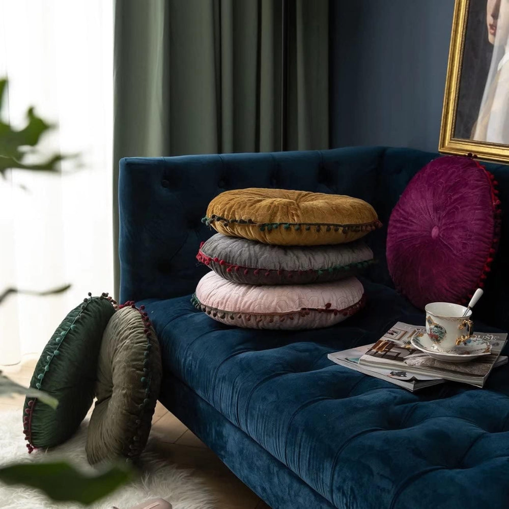 Round velvet cushions stacked and leaning on a navy sofa and on the floor