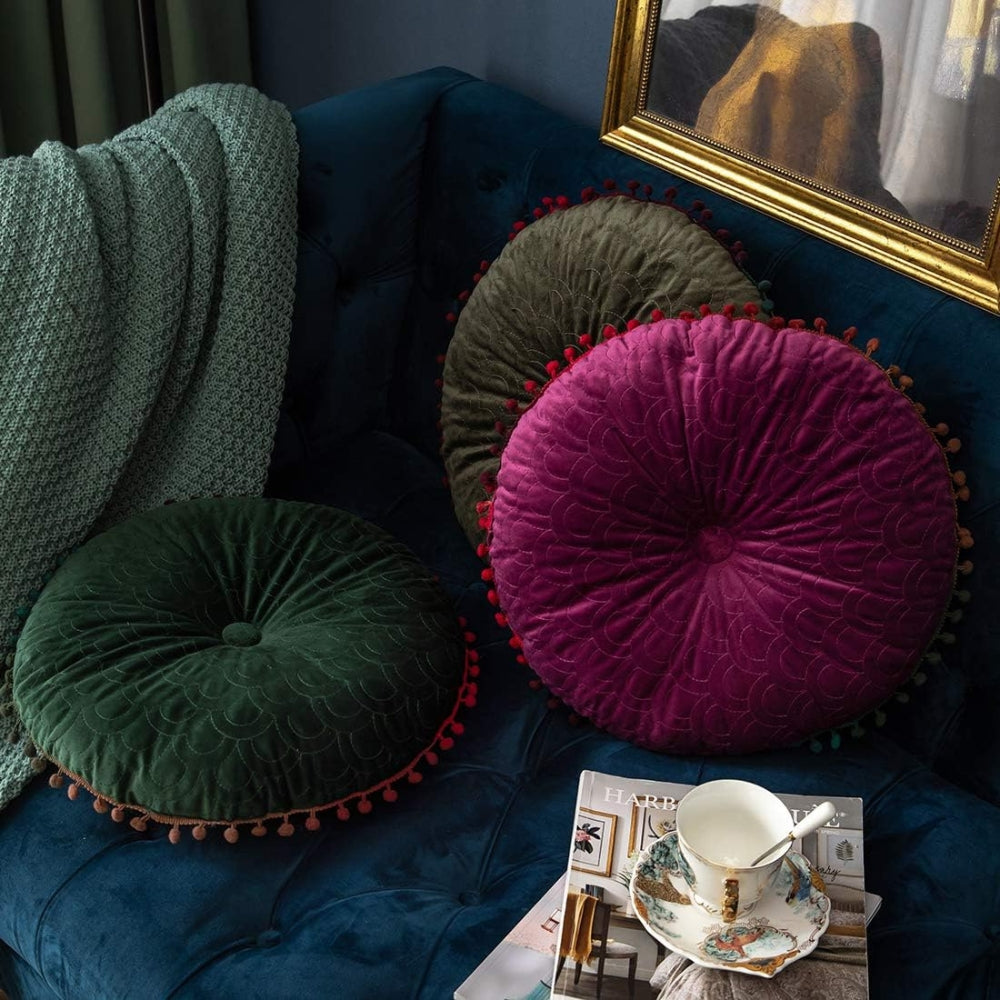 Green round cushion lying on a navy sofa with a plum cushion standing behind it