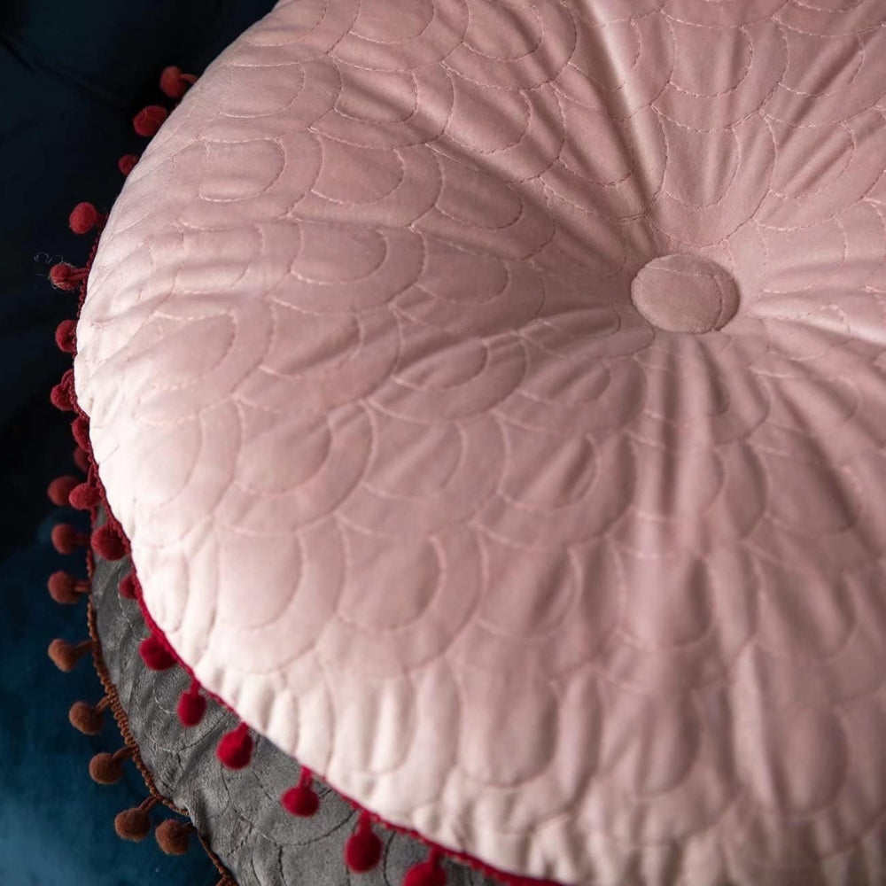 Close-up of the pink cushion's covered button, scallop quilting and pom-pom edge