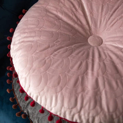 Close-up of the pink cushion's covered button, scallop quilting and pom-pom edge