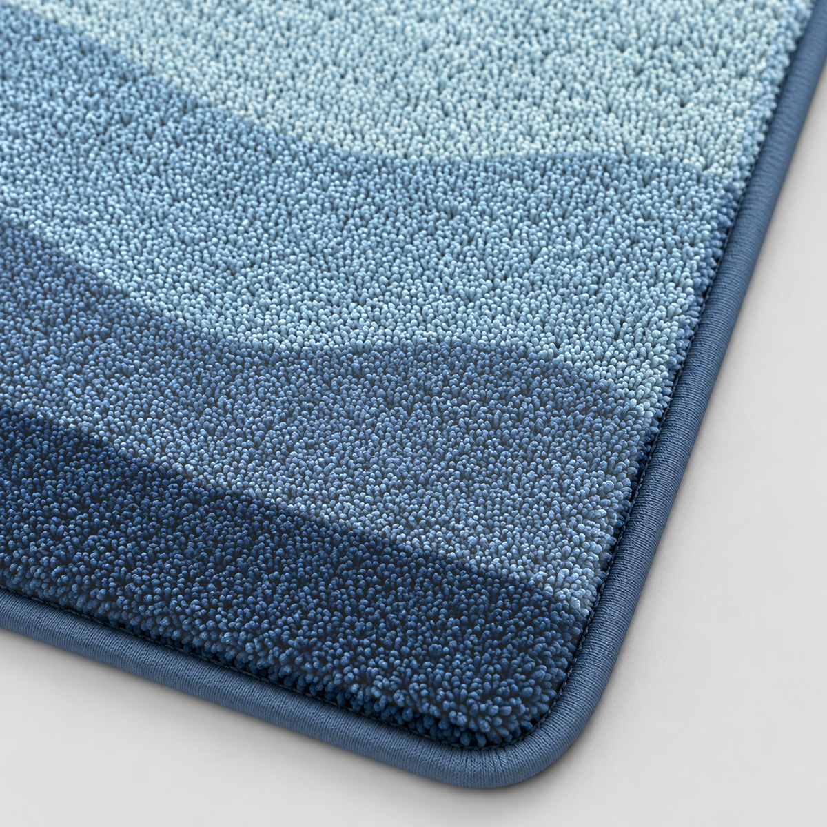 Close-up of the blue bath mat's soft tufted pile in sky blue, denim and navy with a bound edge
