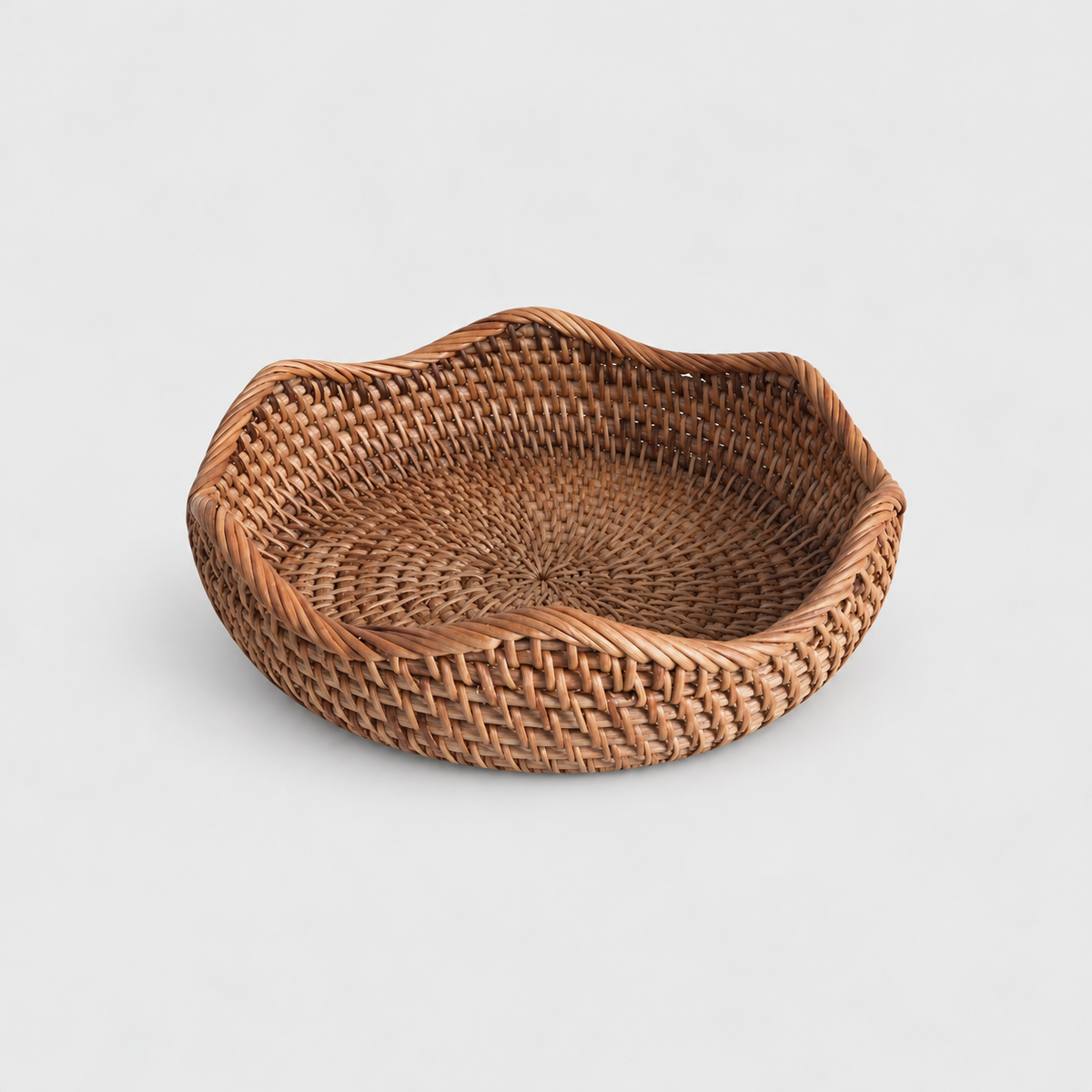 Small shallow round rattan basket with a wavy rope-wrapped rim on a light gray background