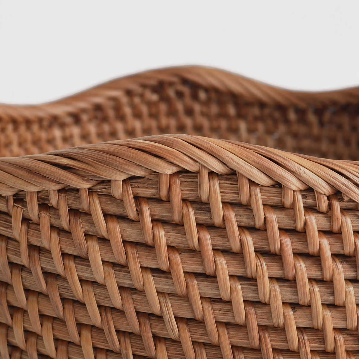 Close-up of the basket's wavy rim wrapped in diagonal rattan strands above rows of slanted stitches