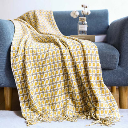 Mustard and gray grid pattern knit throw draped over a blue sofa with tassels on the rug