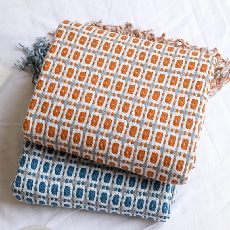 Caramel and blue geometric knit throw blankets folded and stacked on a white bed