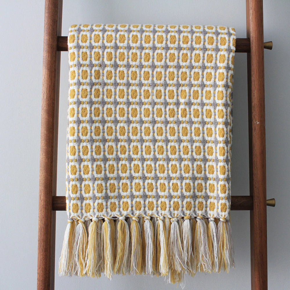 Mustard grid knit throw hanging from a wooden blanket ladder with a full row of tassels
