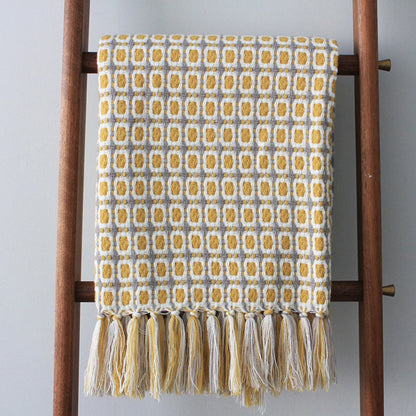 Mustard grid knit throw hanging from a wooden blanket ladder with a full row of tassels