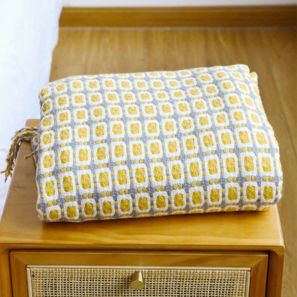 Folded mustard knit throw with a gray and white grid pattern on a wooden cabinet