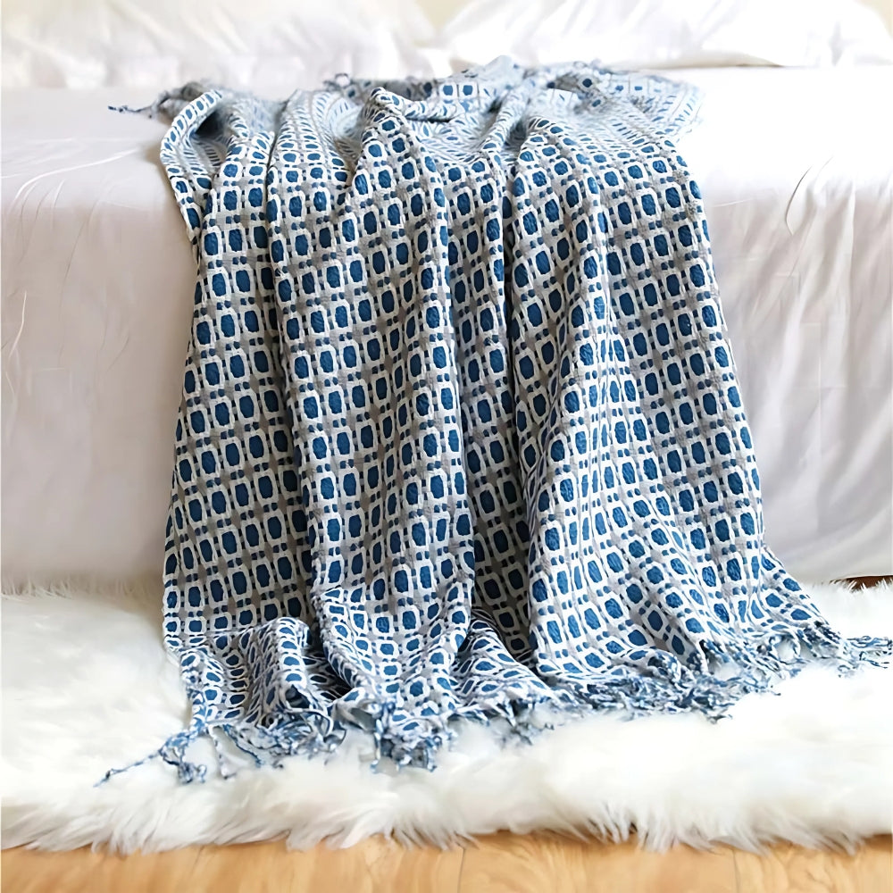 Blue geometric knit throw blanket draped over the end of a bed onto a white rug