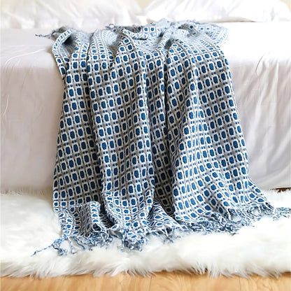Blue geometric knit throw blanket draped over the end of a bed onto a white rug