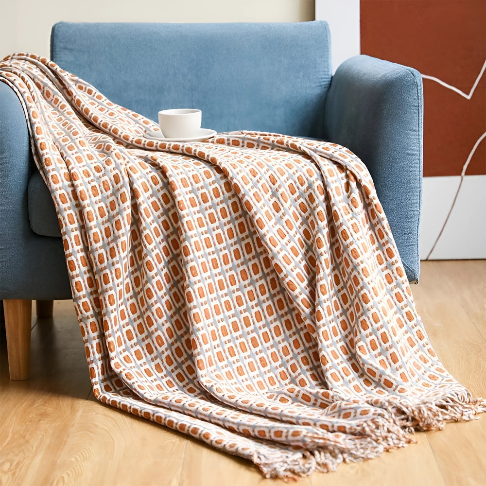 Caramel geometric knit throw blanket draped over a blue armchair with tassels on a wood floor