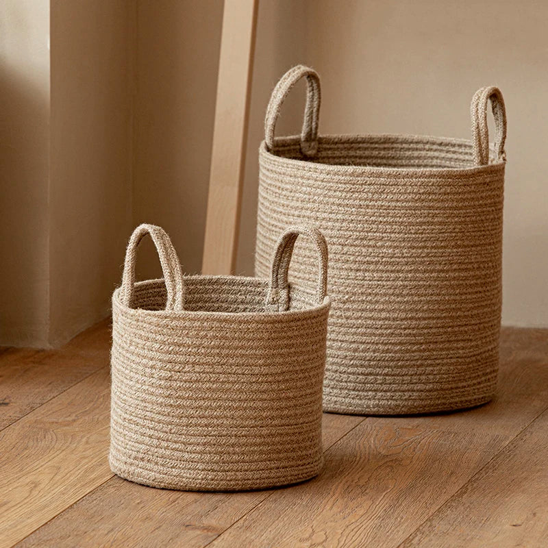 Small and medium tan cotton rope baskets with upright rope handles on a wood floor beside a pale wall