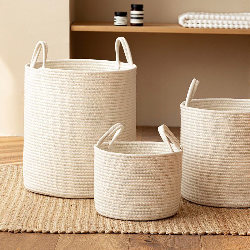 Three white cotton rope baskets in different sizes on a jute rug under a wooden shelf with towels and jars
