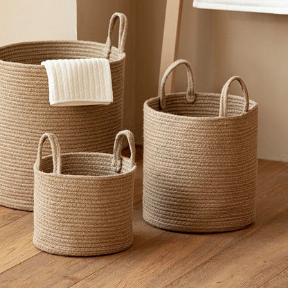 Three tan cotton rope baskets in three sizes on a wood floor, a white towel over the tallest