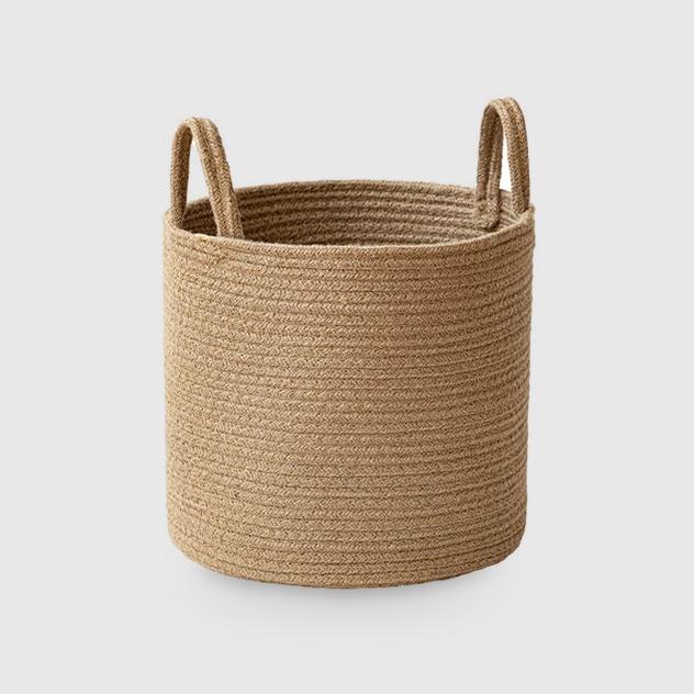 Small round tan cotton rope storage basket with two rope loop handles standing up from the rim, on a light gray studio background