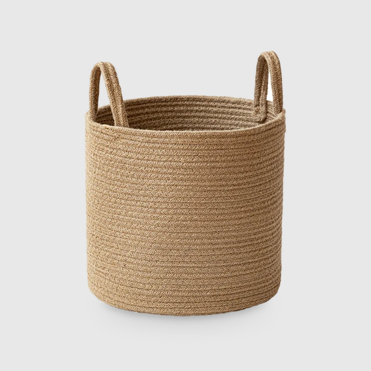Medium round tan cotton rope storage basket with two upright rope handles, on a light gray studio background