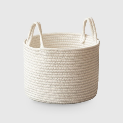 Small round white cotton rope storage basket with two upright rope loop handles, on a light gray studio background