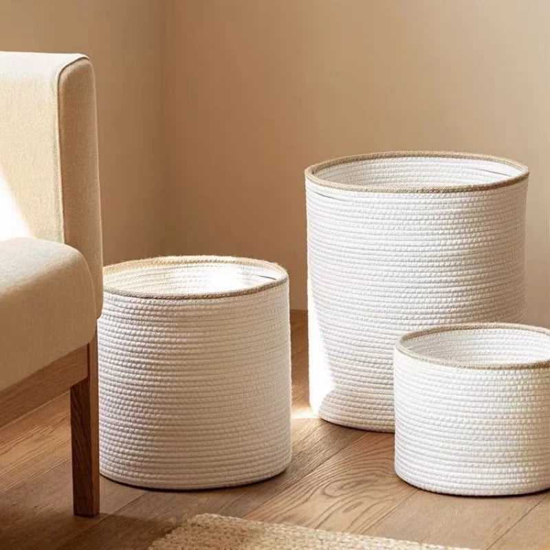 Three white rope baskets with beige rims in small, medium and large beside an armchair in a warm living room