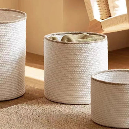 White cotton rope baskets with beige rims on a jute rug in low sunlight, one holding a folded green blanket