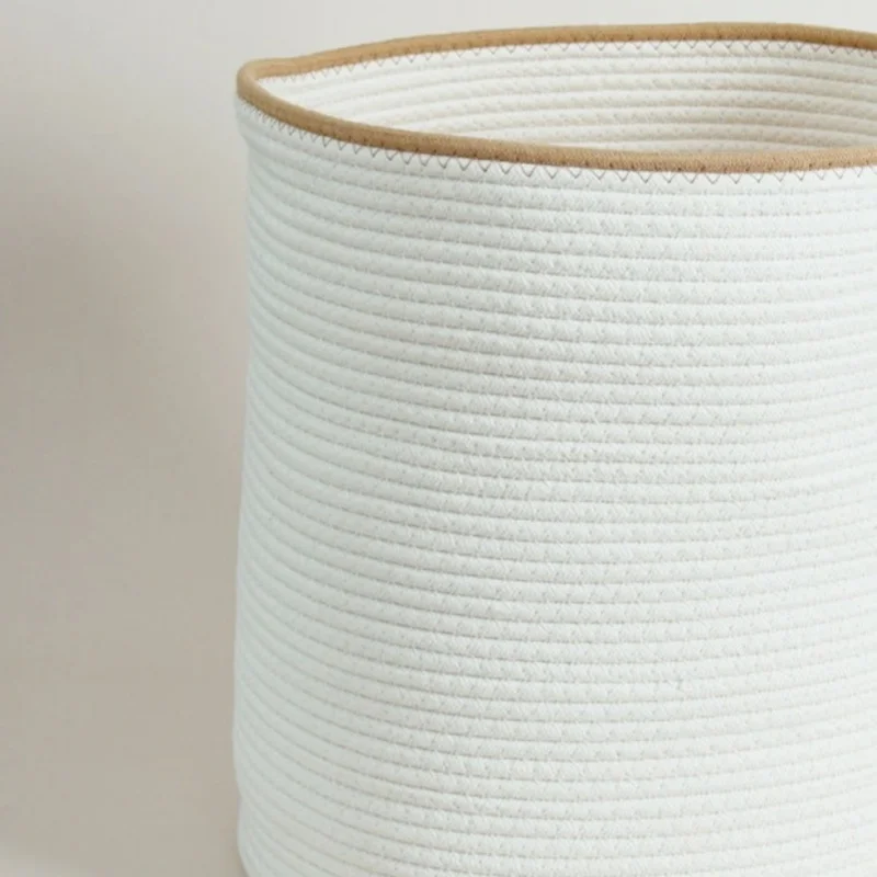 Close-up of the white rope basket's tan rim and zigzag stitch above rows of coiled white cotton rope