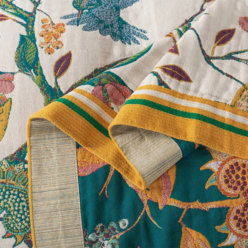 Close-up of the woven floral coverlet showing the cream front, the teal back and the striped border