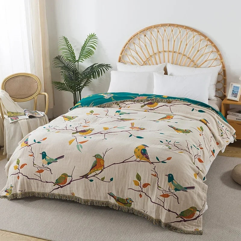 Cream cotton coverlet with songbirds on branches and a fringed edge spread over a bed