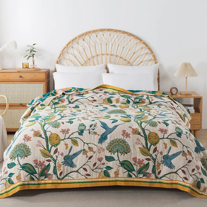 Cream floral cotton coverlet with green branches and blue hummingbirds spread over a bed