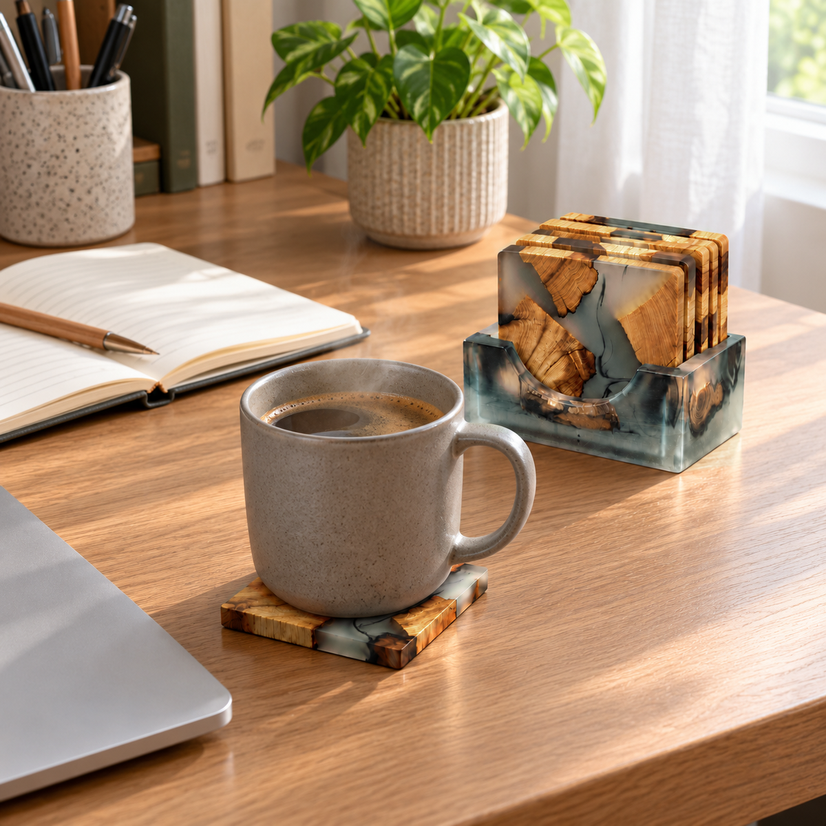 Coffee mug on a resin and wood coaster on an oak desk beside a laptop and notebook, the holder with five more coasters behind