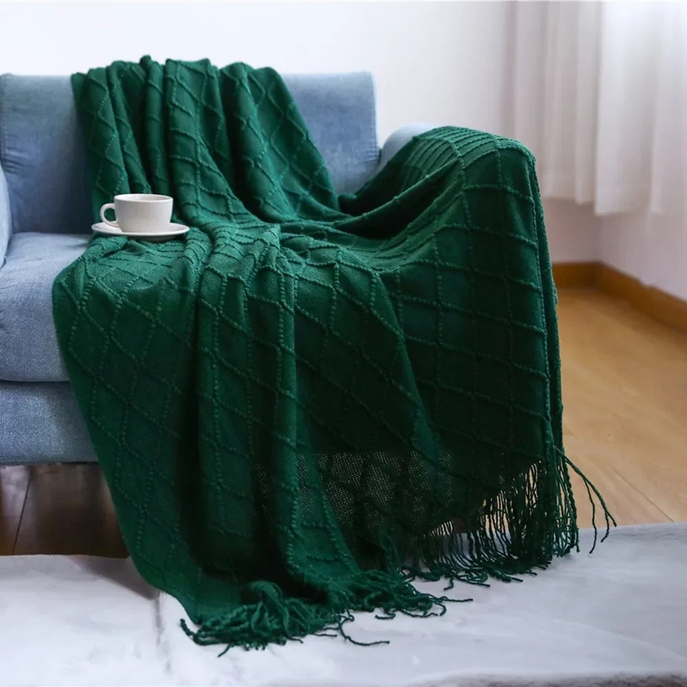 Green knit throw with a raised diamond lattice draped over a blue sofa, tassels resting on the rug