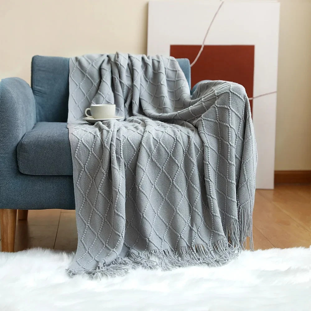 Light gray knit throw blanket with raised diamond texture draped over a blue sofa onto a white rug