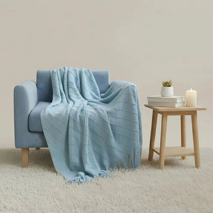 Pale blue diamond knit throw draped over an armchair beside a small wooden side table