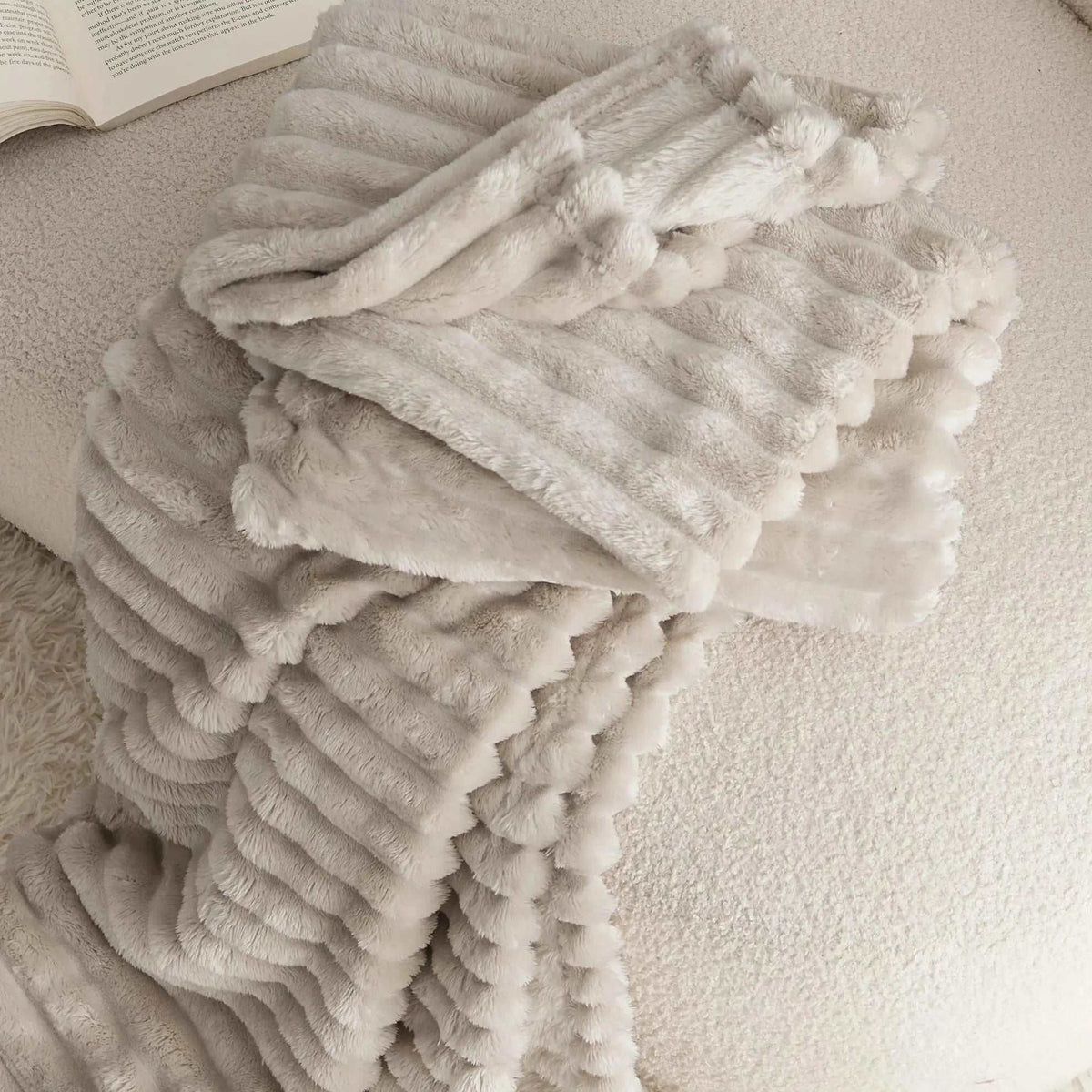 Close-up of the beige faux rabbit fur throw folded on a seat, showing the soft pile and rounded pleat ends