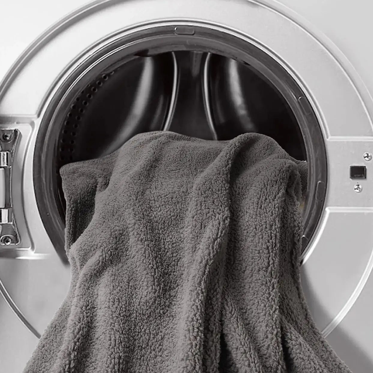 Gray sherpa blanket hanging out of the open door of a front-loading washing machine